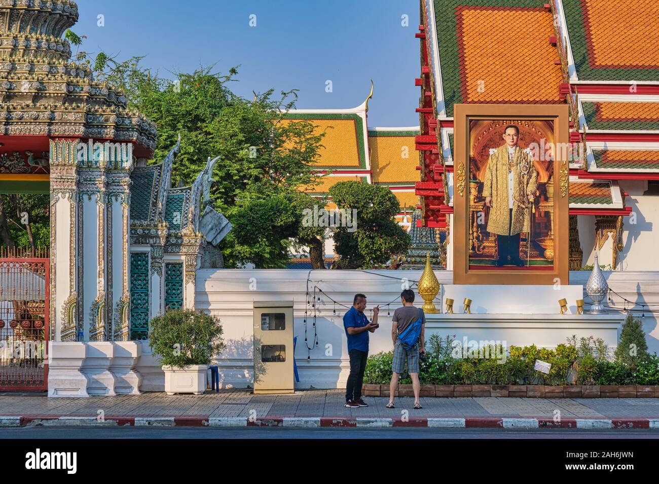 Sous un portrait de la fin du roi Bhumipol, Aduladej thaïlandais le long du mur oriental de Wat Po (PHO), Bangkok, Thaïlande, un tuk-tuk driver parle à un touriste Banque D'Images