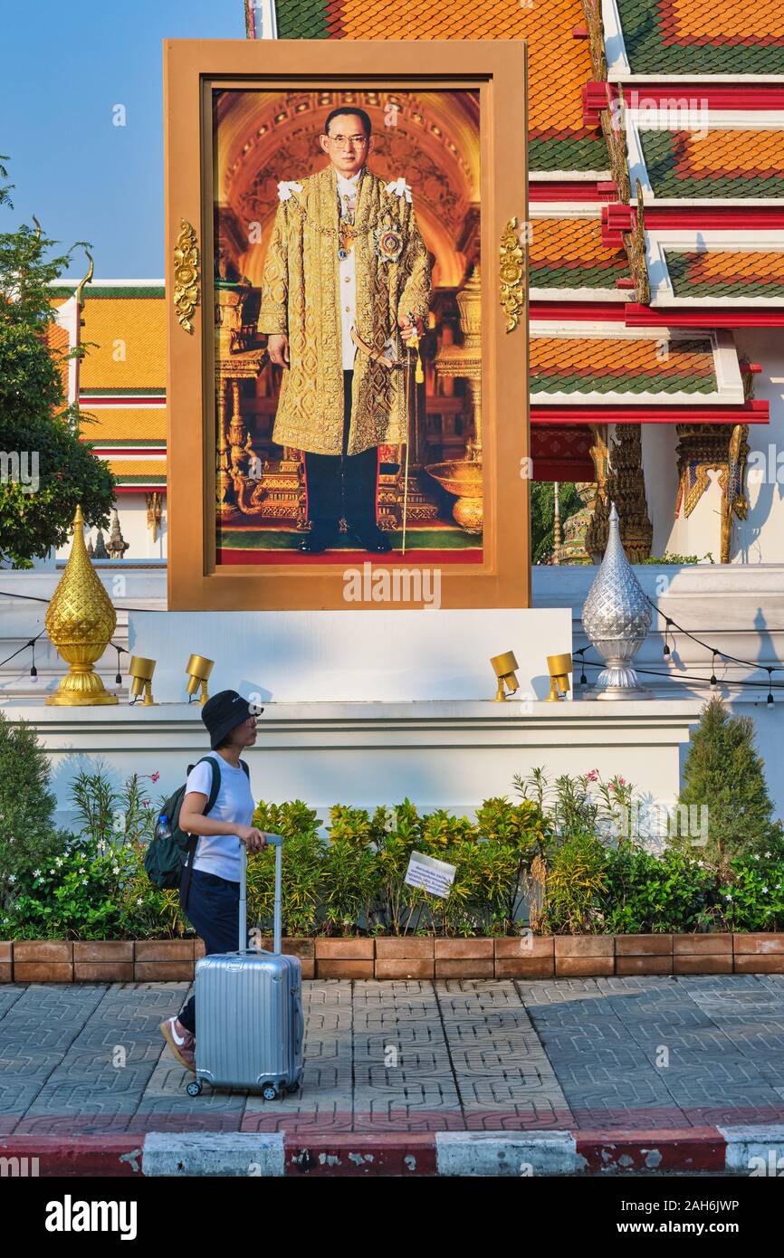Une femme touriste avec valise passe sous un portrait de la fin du roi Bhumipol, Aduladej thaïlandais le long du mur oriental de Wat Po (PHO), Bangkok, Thaïlande Banque D'Images