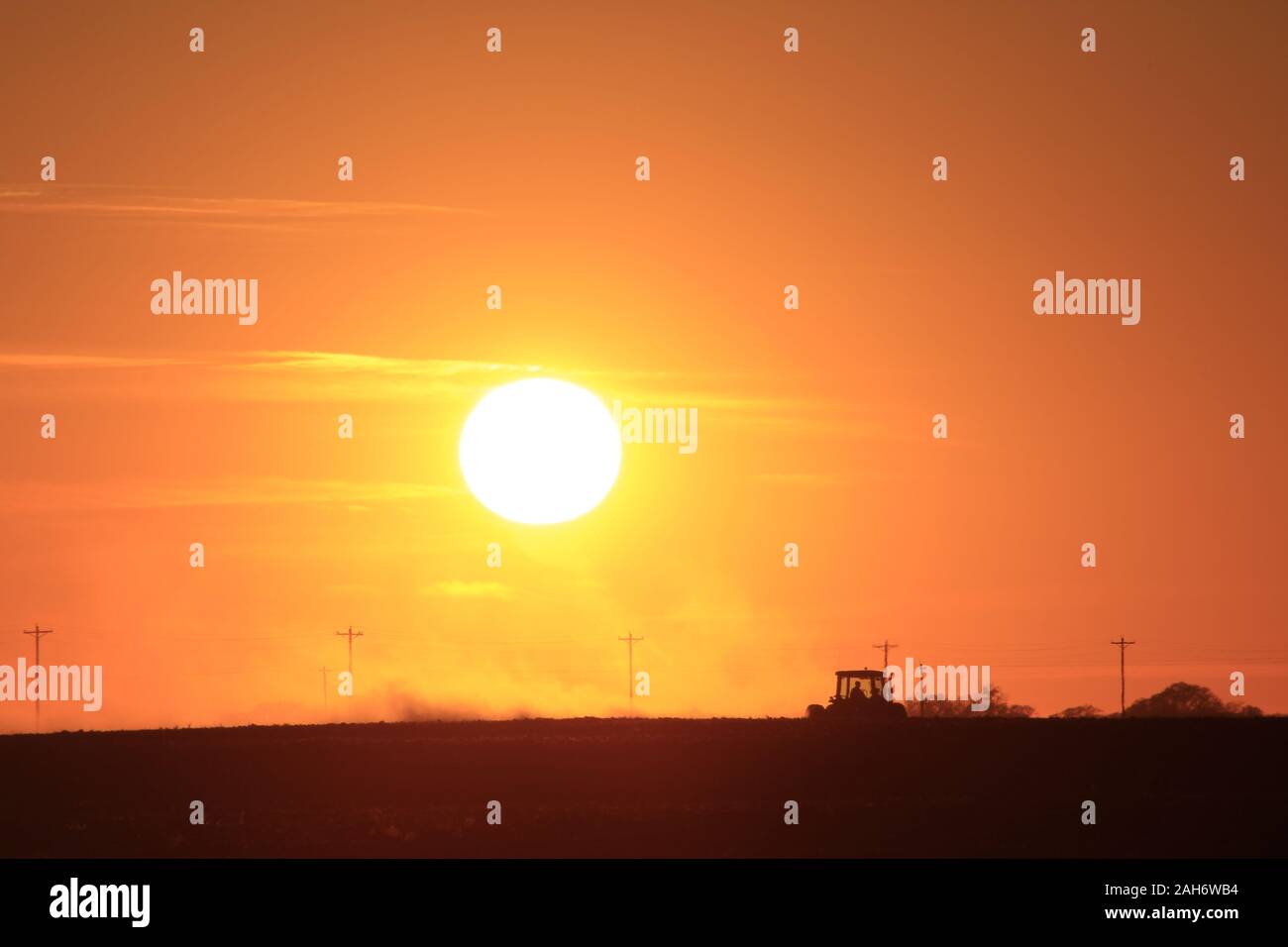 Orange flamboyant Kansas Coucher du soleil avec un exploitant agricole travaillant son domaine à la campagne dans le Kansas. Banque D'Images