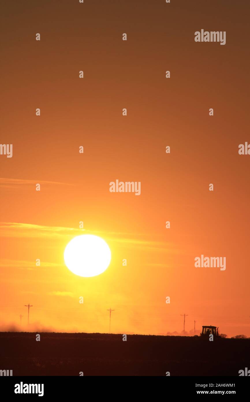 Orange flamboyant Kansas Coucher du soleil avec un exploitant agricole travaillant son domaine à la campagne dans le Kansas. Banque D'Images