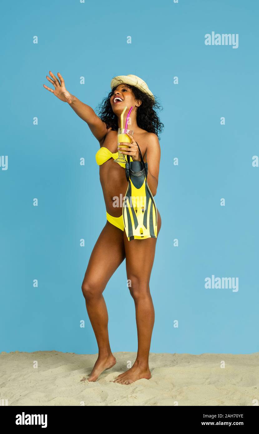 Prêt à nager. Happy young woman with cocktail et des palmes sur fond studio bleu. Concept d'émotions humaines, expression du visage, vacances d'été ou de fin de semaine. Chill, été, mer, océan. Banque D'Images