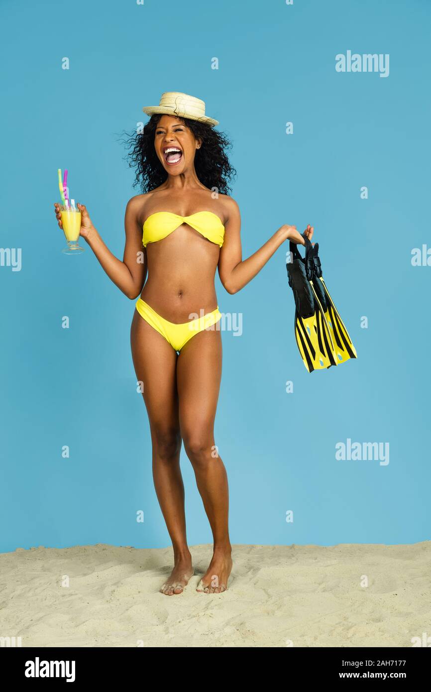 Le bonheur. Happy young woman with cocktail et des palmes sur fond studio bleu. Concept d'émotions humaines, expression du visage, vacances d'été ou de fin de semaine. Chill, été, mer, océan. Banque D'Images