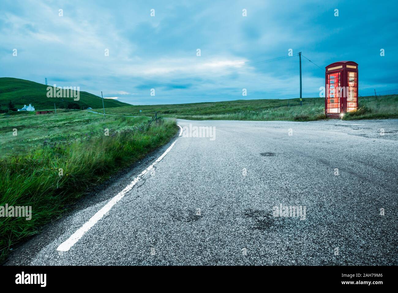 Sur une route rurale écossaise la nuit, se trouve une cabine téléphonique britannique solitaire rouge, au bord du trottoir Banque D'Images