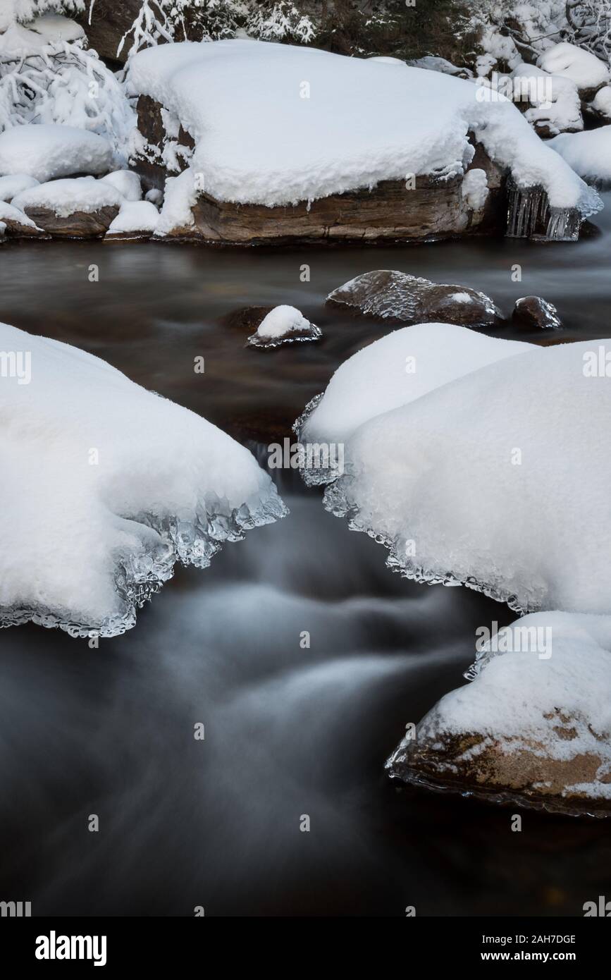 Vue rapprochée du paysage hivernal, avec un ruisseau d'eau froide qui coule entre des rochers enneigés et dans les rapides Banque D'Images