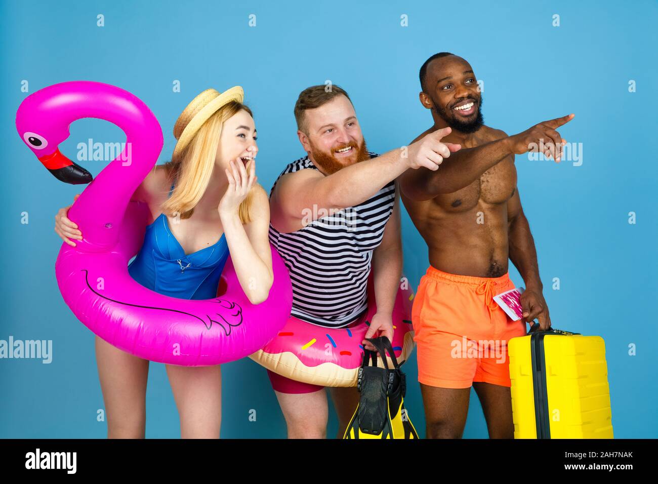 Préparé pour le voyage. Heureux les jeunes amis se reposer et en pointant sur l'arrière-plan studio bleu. Concept d'émotions humaines, expression du visage, vacances d'été ou de fin de semaine. Chill, été, mer, océan. Banque D'Images