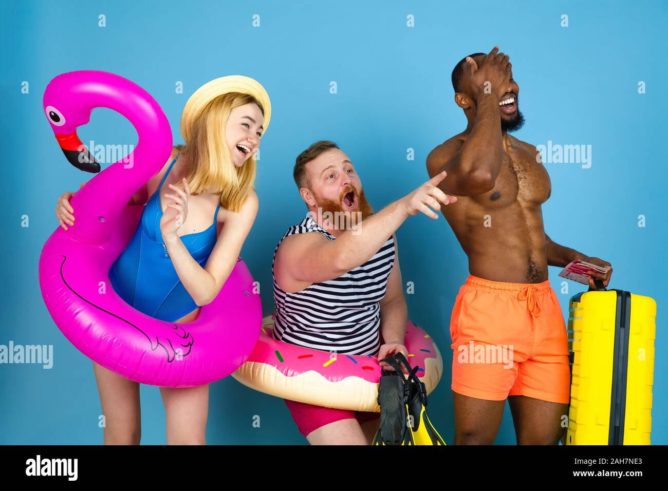 Préparé pour le voyage. Heureux les jeunes amis se reposer et en pointant sur l'arrière-plan studio bleu. Concept d'émotions humaines, expression du visage, vacances d'été ou de fin de semaine. Chill, été, mer, océan. Banque D'Images