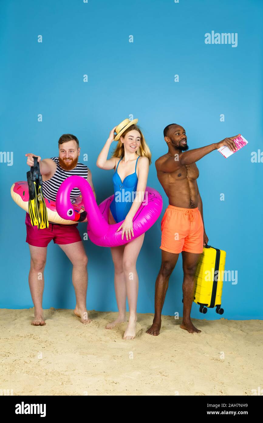 Préparé pour le voyage. Heureux les jeunes amis se reposer et en pointant sur l'arrière-plan studio bleu. Concept d'émotions humaines, expression du visage, vacances d'été ou de fin de semaine. Chill, été, mer, océan. Banque D'Images