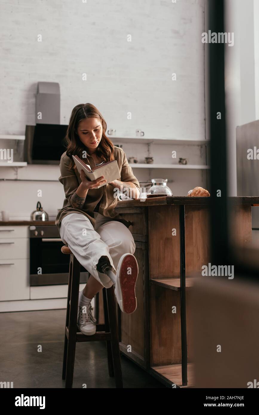 Belle femme avec prothèse lecture livre par table de cuisine Banque D'Images