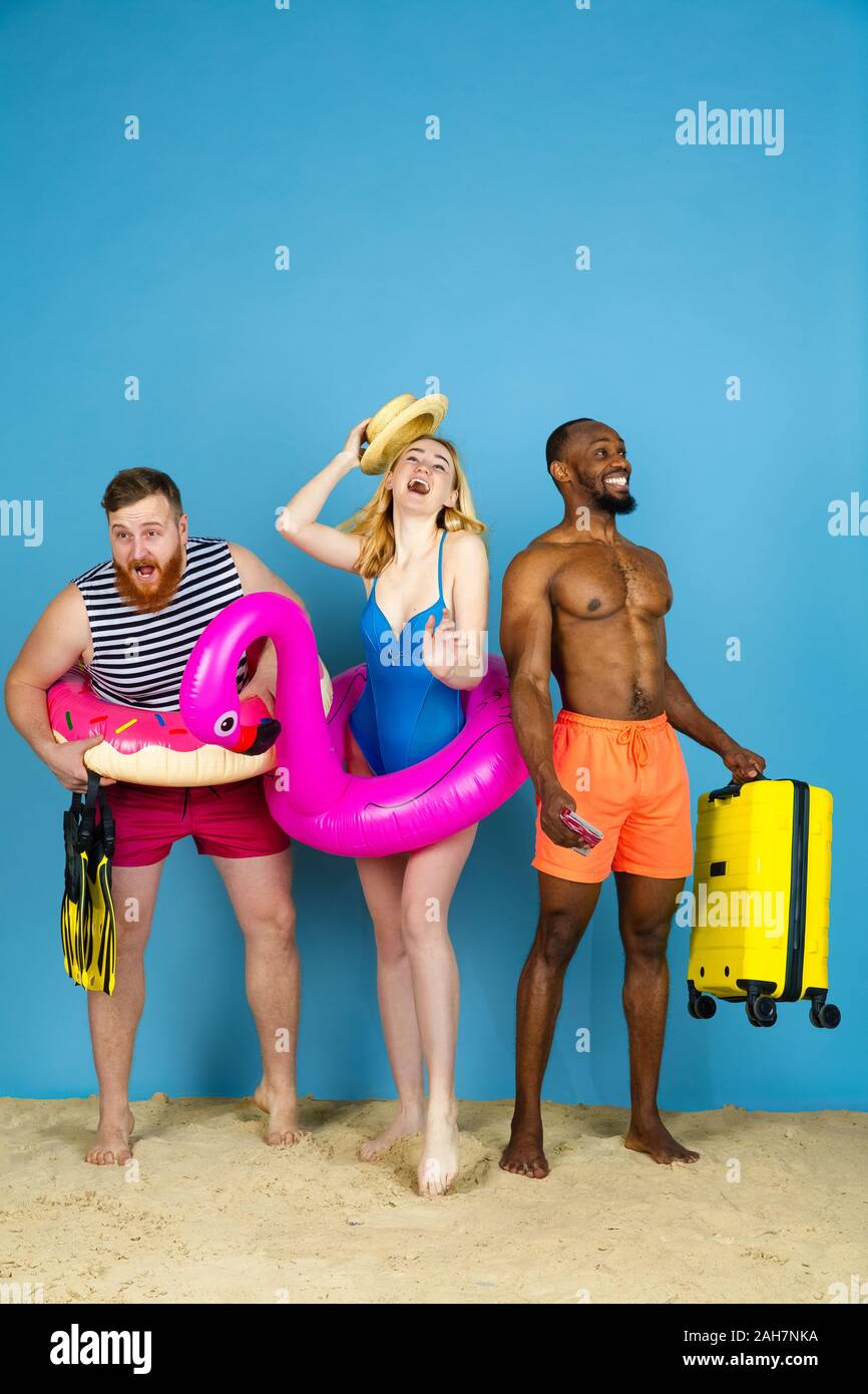 Préparé pour le voyage. Heureux les jeunes amis se reposer et regarder étonné sur fond studio bleu. Concept d'émotions humaines, expression du visage, vacances d'été ou de fin de semaine. Chill, été, mer, océan. Banque D'Images