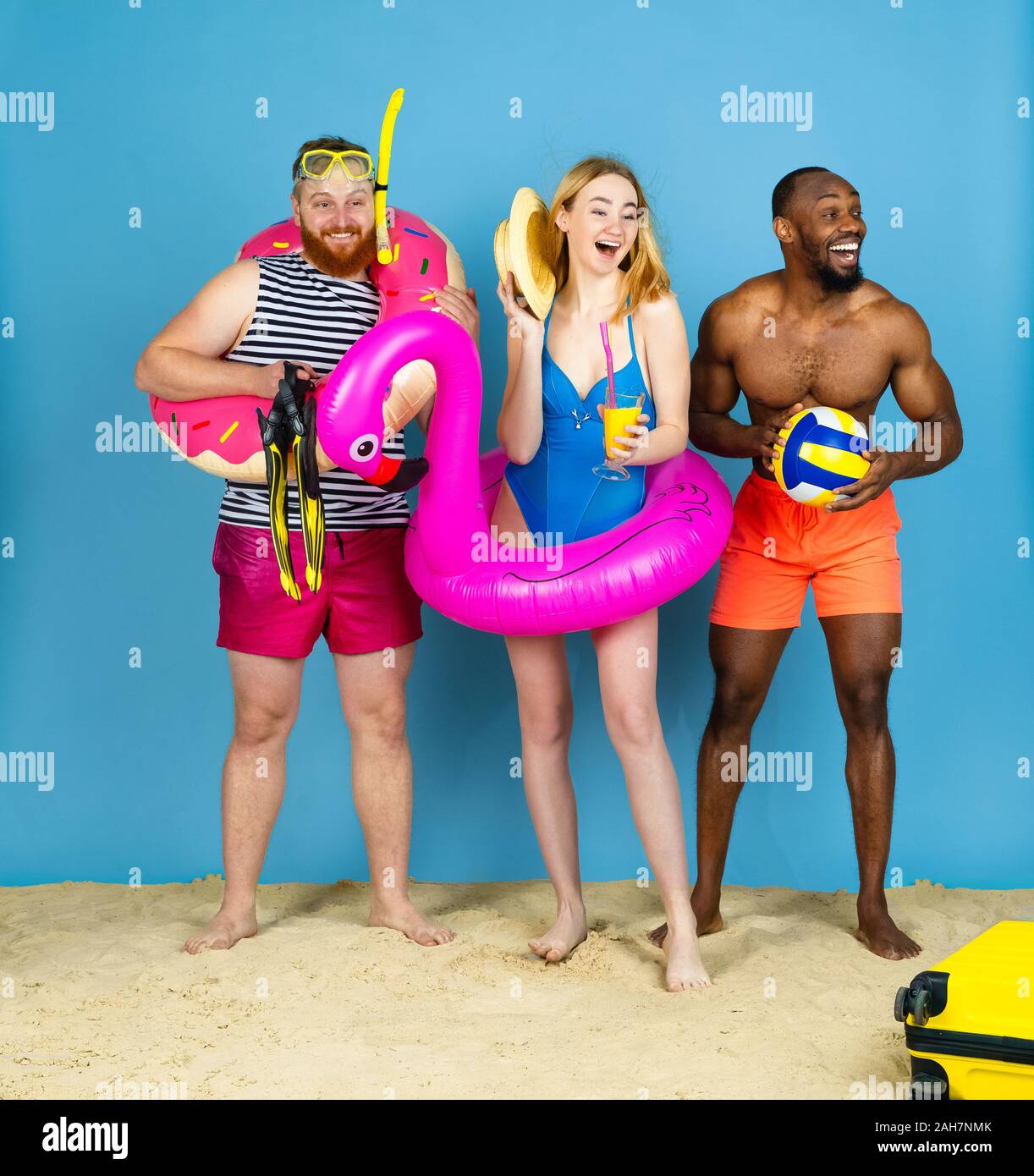 Préparé pour le voyage. Heureux les jeunes amis se reposer et regarder étonné sur fond studio bleu. Concept d'émotions humaines, expression du visage, vacances d'été ou de fin de semaine. Chill, été, mer, océan. Banque D'Images