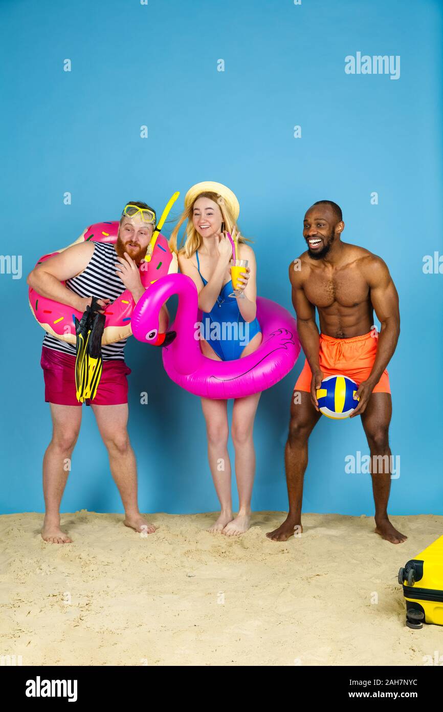 Préparé pour le voyage. Heureux les jeunes amis se reposer et regarder étonné sur fond studio bleu. Concept d'émotions humaines, expression du visage, vacances d'été ou de fin de semaine. Chill, été, mer, océan. Banque D'Images