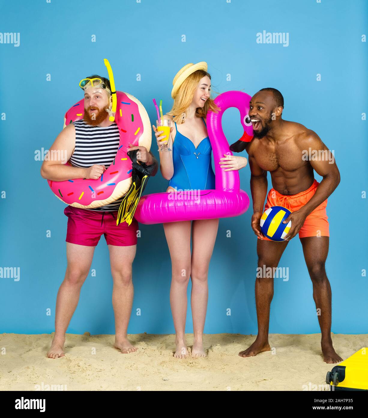 Préparé pour le voyage. Heureux les jeunes amis se reposer et regarder étonné sur fond studio bleu. Concept d'émotions humaines, expression du visage, vacances d'été ou de fin de semaine. Chill, été, mer, océan. Banque D'Images