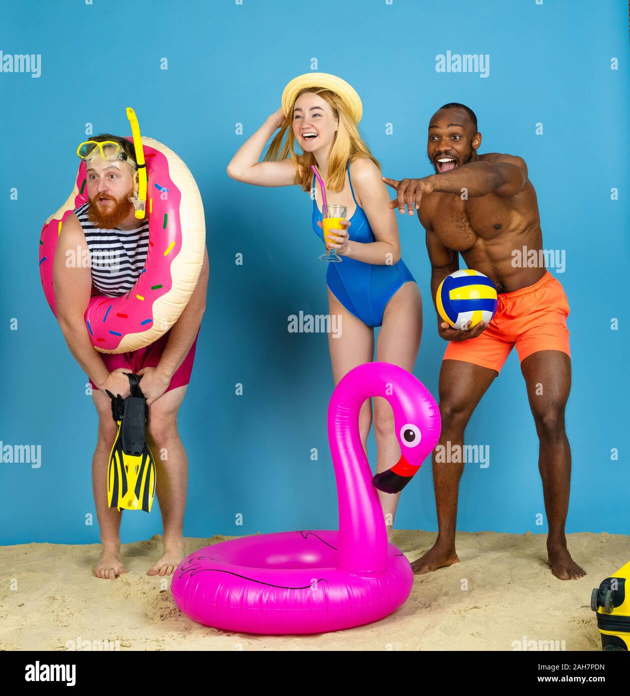 Pointant, laughting. Jeunes amis heureux repos et l'air heureux sur fond studio bleu. Concept d'émotions humaines, expression du visage, vacances d'été ou de fin de semaine. Chill, été, mer, océan. Banque D'Images