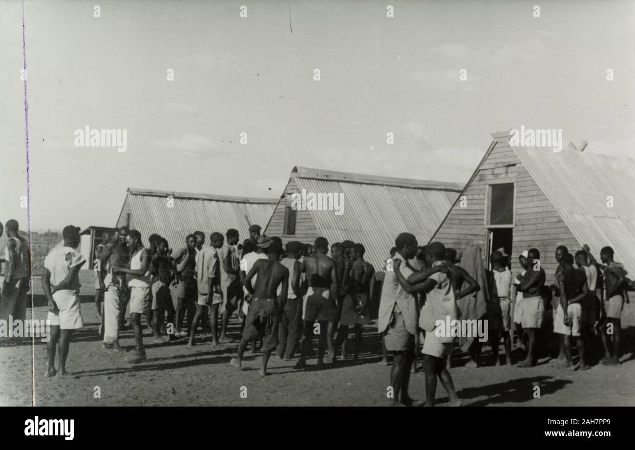 Au Kenya, les jeunes hommes se réunissent à côté de Kikuyu abris préfabriqués, un camp d'hébergement temporaire pour la Home Guard Kikuyu. Manuscrit original description : hébergement temporaire, 1953 KG. 1995/076/1/1/15/8.26. Banque D'Images