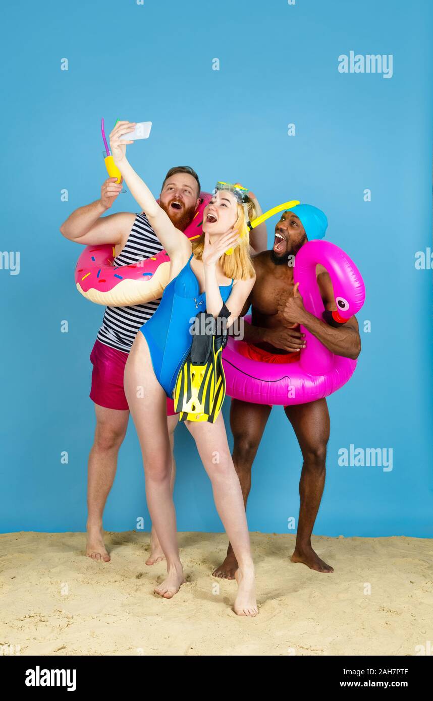 Tourné pour la mémoire. Happy friends se reposer et prendre ou selfies vlog sur fond studio bleu. Concept d'émotions humaines, expression du visage, vacances d'été ou de fin de semaine. Chill, été, mer, océan. Banque D'Images