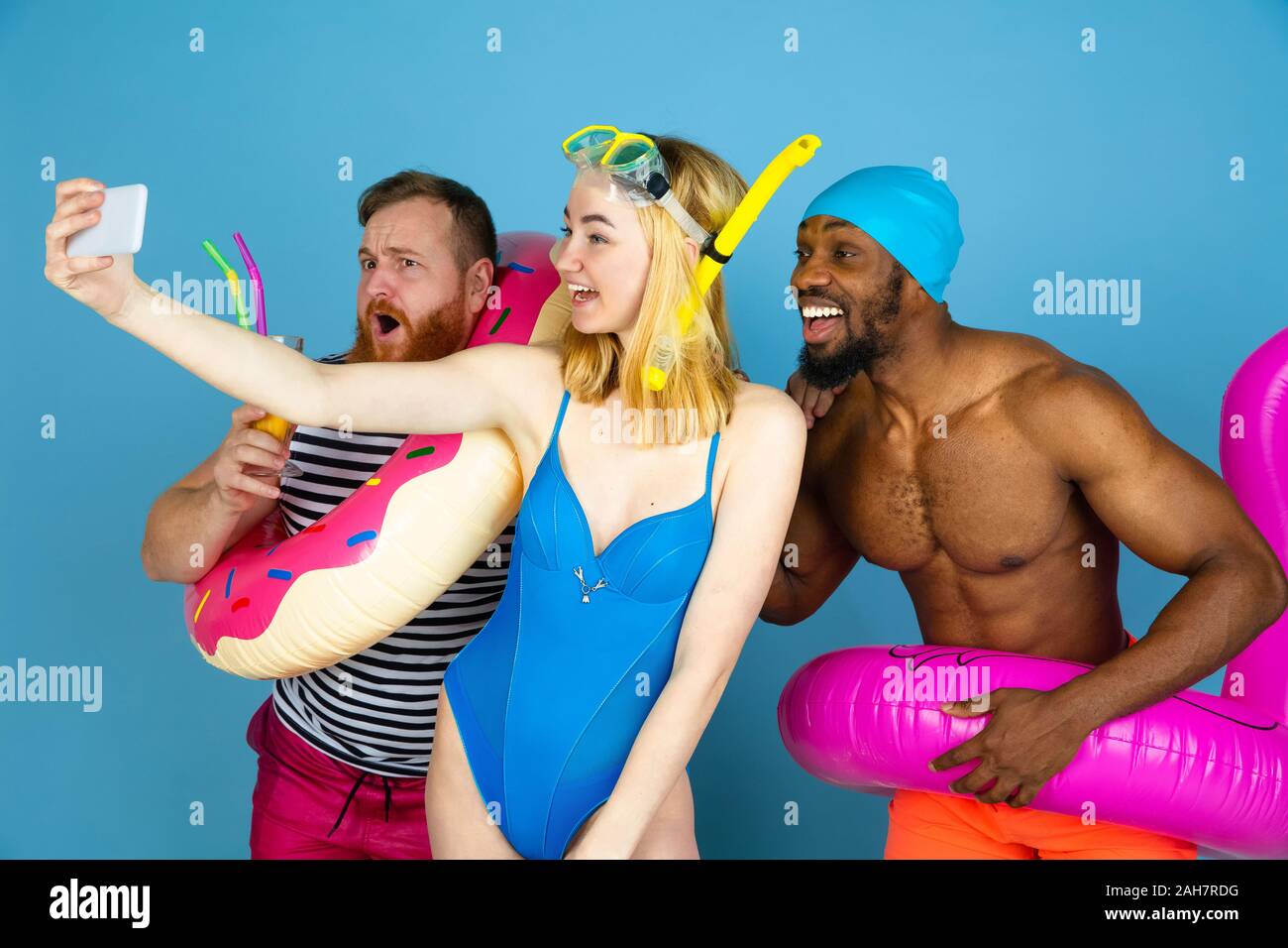 Tourné pour la mémoire. Happy friends se reposer et prendre ou selfies vlog sur fond studio bleu. Concept d'émotions humaines, expression du visage, vacances d'été ou de fin de semaine. Chill, été, mer, océan. Banque D'Images