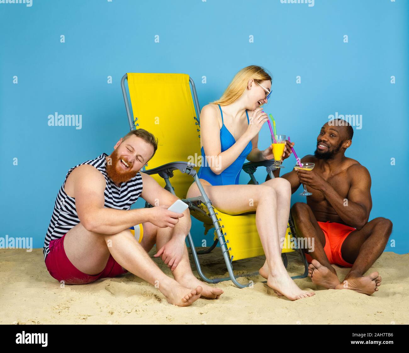 Temps lumineux. Happy friends se reposer, boire des cocktails sur fond studio bleu. Concept d'émotions humaines, expression du visage, vacances d'été ou de fin de semaine. Chill, été, mer, océan, l'alcool. Banque D'Images