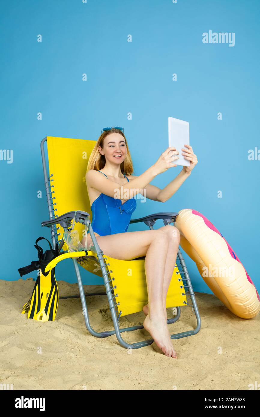 Happy young woman with tablet selfies prend ou vlog sur les voyages sur fond studio bleu. Concept d'émotions humaines, l'expression du visage, vacances, week-end d'été. L'été, mer, océan, l'alcool. Banque D'Images