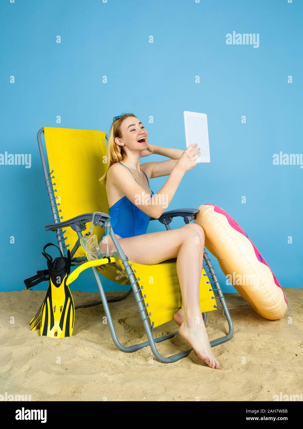 Happy young woman with tablet selfies prend ou vlog sur les voyages sur fond studio bleu. Concept d'émotions humaines, l'expression du visage, vacances, week-end d'été. L'été, mer, océan, l'alcool. Banque D'Images