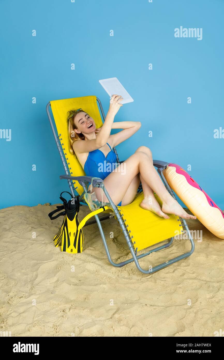 Happy young woman with tablet selfies prend ou vlog sur les voyages sur fond studio bleu. Concept d'émotions humaines, l'expression du visage, vacances, week-end d'été. L'été, mer, océan, l'alcool. Banque D'Images