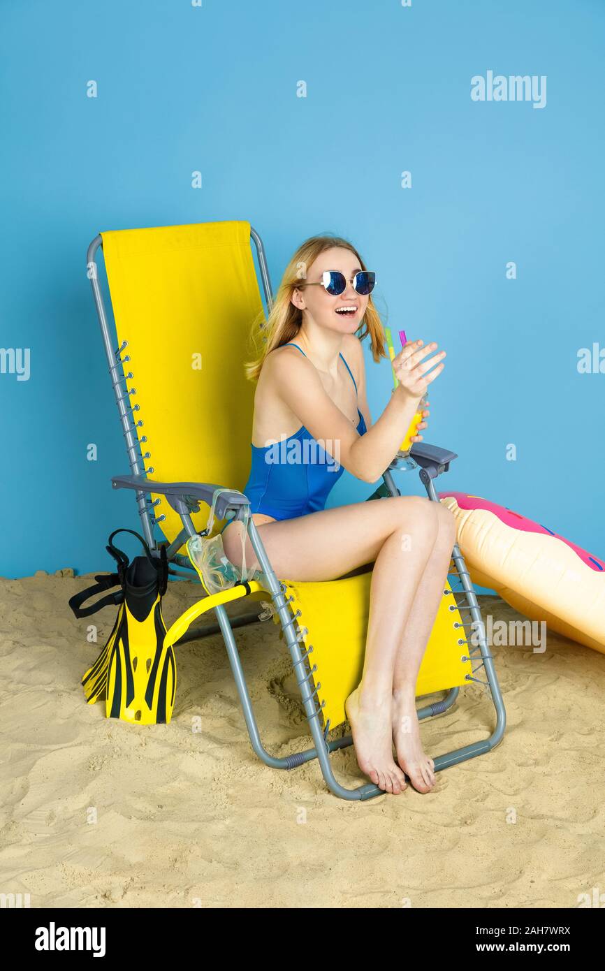 Happy young woman with cocktail smiling, laughting, salut on blue background studio. Concept d'émotions humaines, l'expression du visage, vacances, week-end d'été. L'été, mer, océan, l'alcool. Banque D'Images