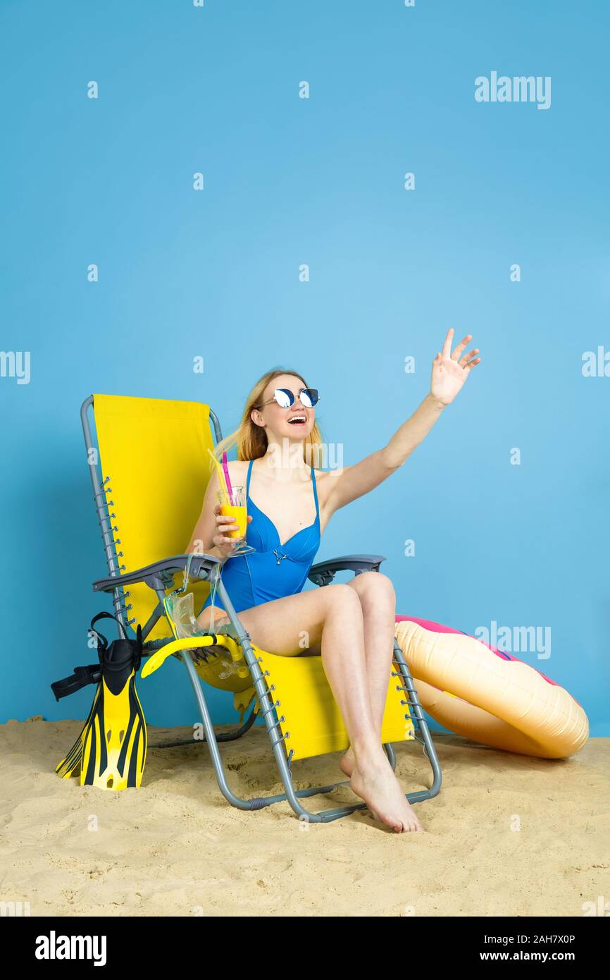 Happy young woman with cocktail smiling, laughting, salut on blue background studio. Concept d'émotions humaines, l'expression du visage, vacances, week-end d'été. L'été, mer, océan, l'alcool. Banque D'Images