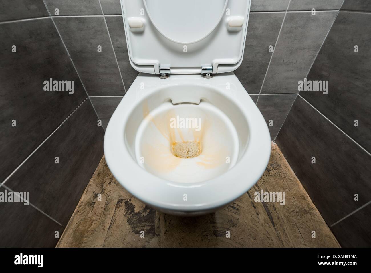 Détergent liquide jaune en céramique dans la cuvette des toilettes propres dans des toilettes modernes avec des carreaux gris Banque D'Images