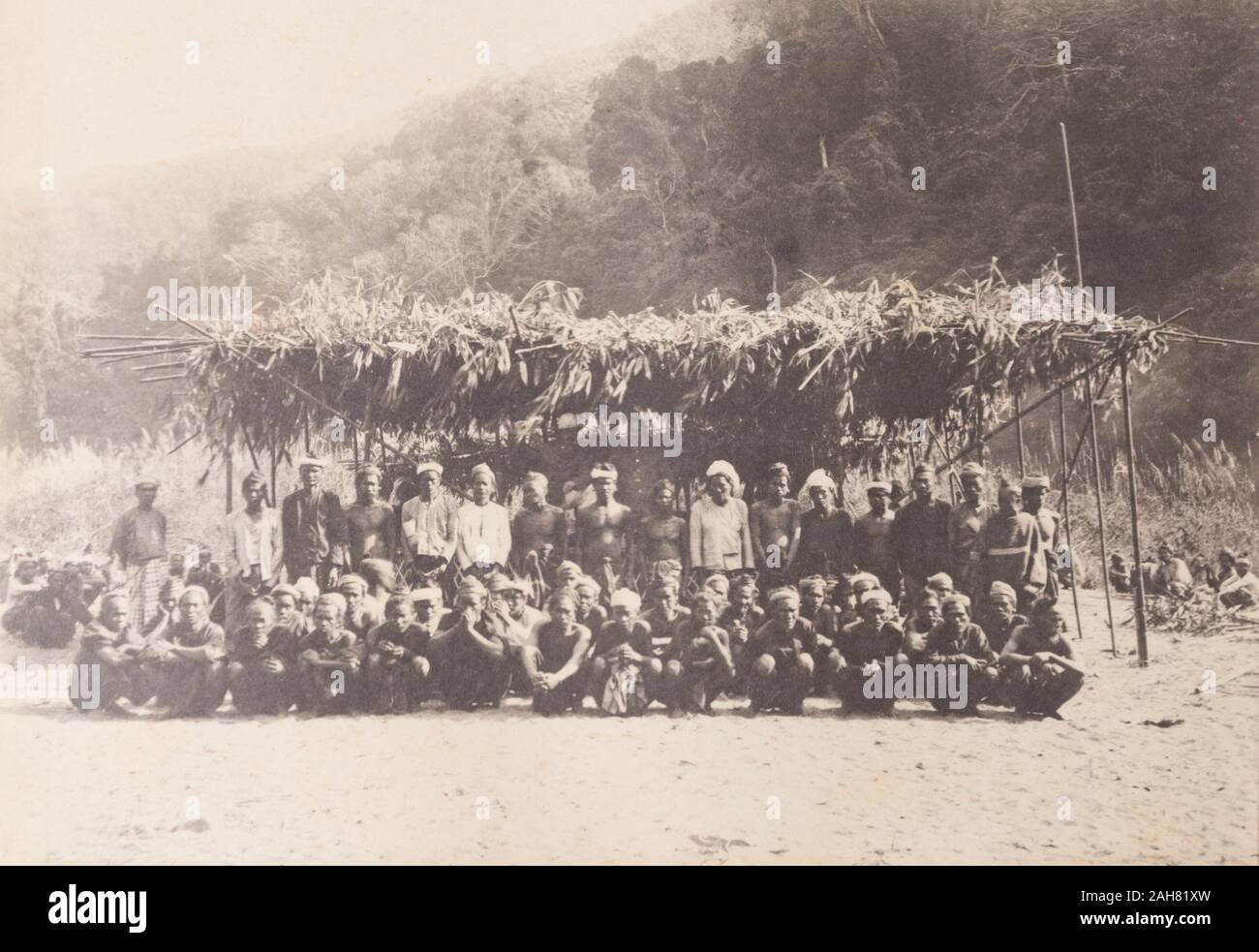 BurmaMyanmar, portrait de groupe de tribus Chin Chin de la collines. Plusieurs dizaines d'hommes s'accroupir ou se tenir dans une clairière de sable sous un toit de fortune, de l'herbe à l'abri. D'autres personnes, peut-être les femmes Chin, sont assis à une distance. Manuscrit original description : Dans l'Arakan Chin Hills, janvier 1897, janvier 1897. 2003/071/1/1/2/41. Banque D'Images