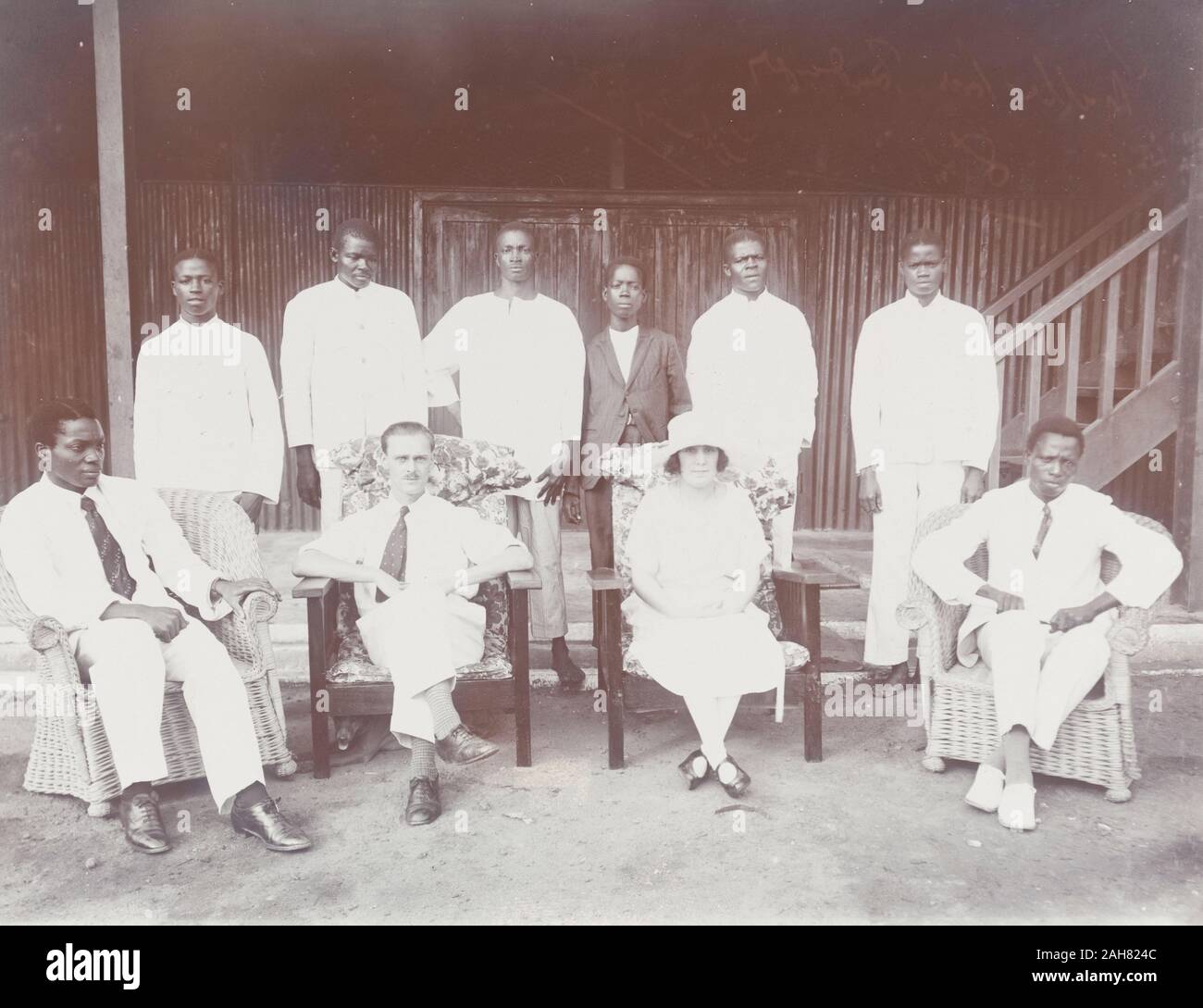 Le Nigeria, Sous-titre suivant : 'Mr et Mme Baxendale de Miller Bros : Le personnel 1924 Badagry'.Mr et Mme Baxendale (centre) pose devant l'appareil photo avec les employés de Miller Brothers & Co. Les six jeunes hommes africains derrière eux sont habillés en blanc pour la plupart, peut-être domestiques ou employés de bureau. Deux hommes dans l'ouest de l'Afrique officielle robe s'asseoir de chaque côté de l'Baxendales dans des fauteuils en rotin, 1924. 1/53/2000/098. Banque D'Images