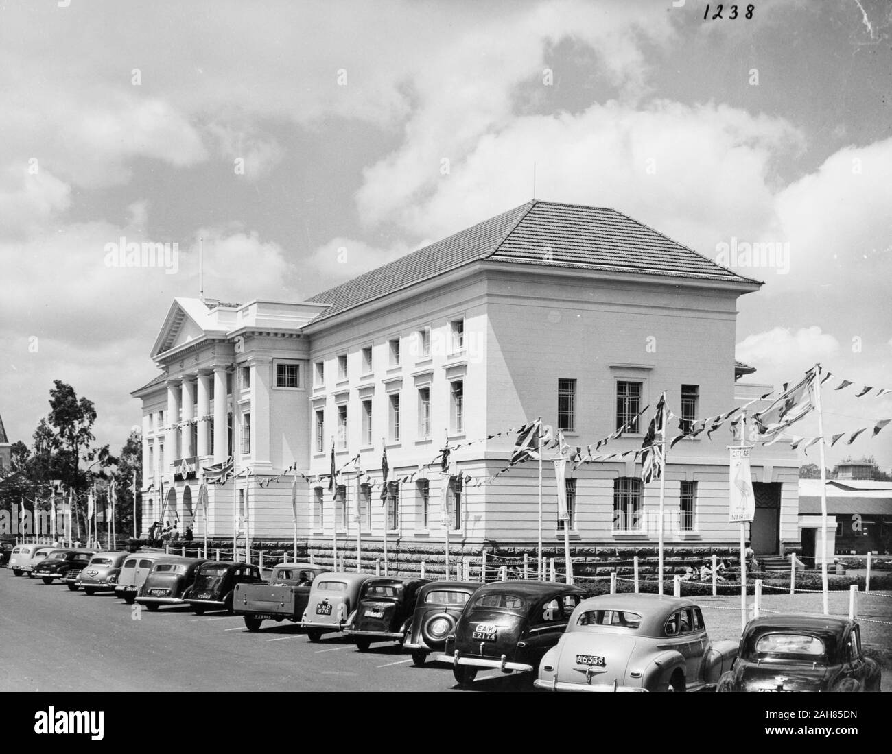 Au Kenya, les élévations de l'avant et du côté de l'Hôtel de ville de Nairobi. L'extérieur du bâtiment sont une ligne de drapeaux portant l'Union Jack avec banderoles et fanions illustrant une autruche avec les mots "VILLE DE NAIROBI.'' un drapeau porte la croix de saint André. Ouvriers peut être vu l'érection d'un drapeau à l'avant de l'Hôtel de Ville. et les voitures longent la rue à l'extérieur, février 1952. 2001/090/1/4/1/58. Banque D'Images