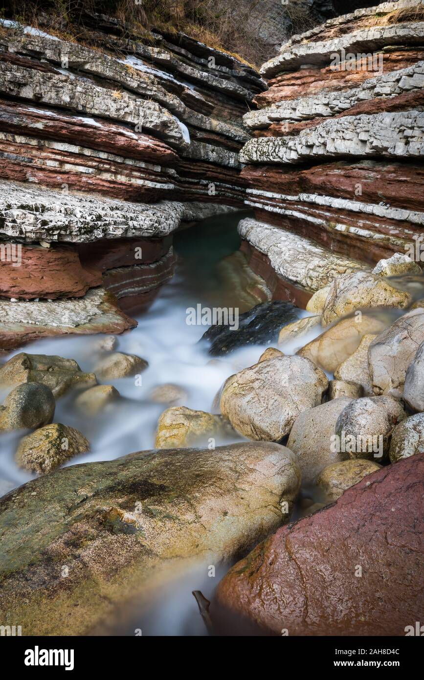 Près de l'entrée d'un canyon de fente en grès rouge stratifié avec de l'eau qui coule sur son fond dans le nord de l'Italie Banque D'Images