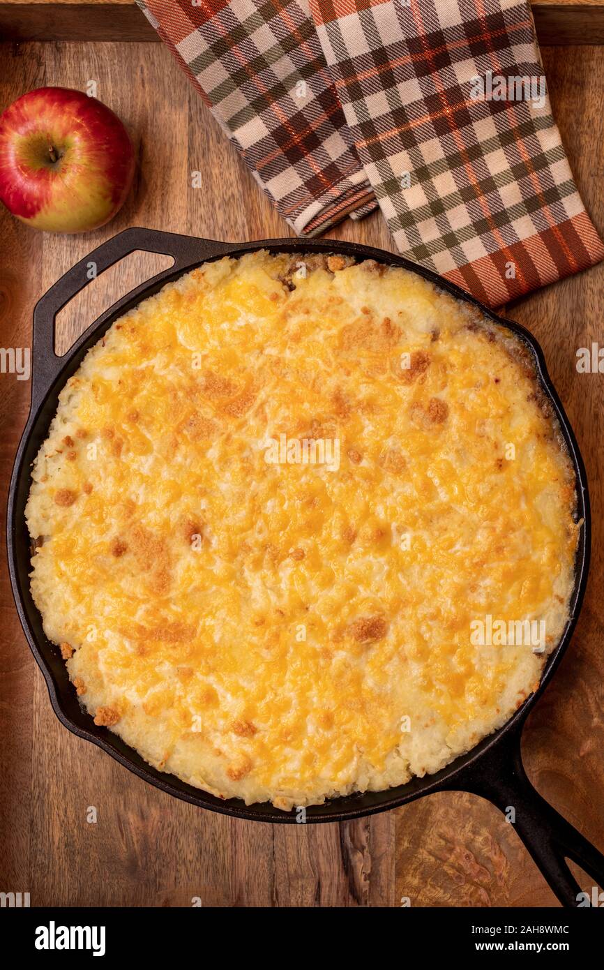 Tarte Shephers au four dans une poêle en fonte et placé sur un plateau de bois avec une pomme et des serviettes Banque D'Images