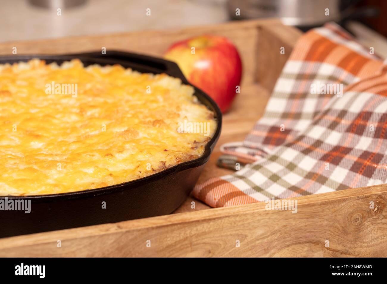 Tarte Shephers au four dans une poêle en fonte et placé sur un plateau de bois avec une pomme et des serviettes Banque D'Images