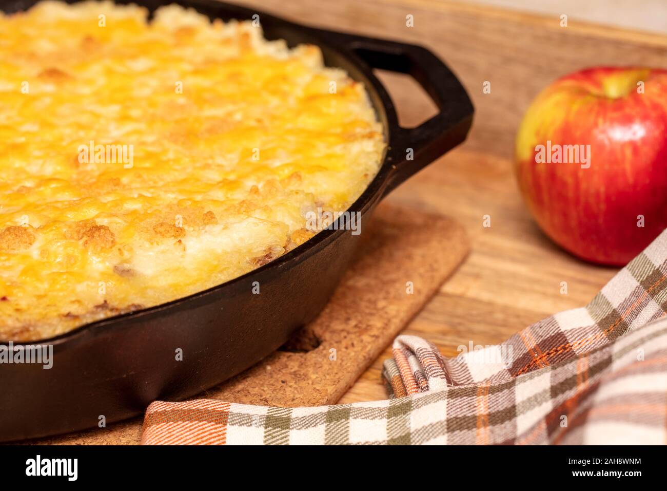 Tarte Shephers au four dans une poêle en fonte et placé sur un plateau de bois avec une pomme et des serviettes Banque D'Images