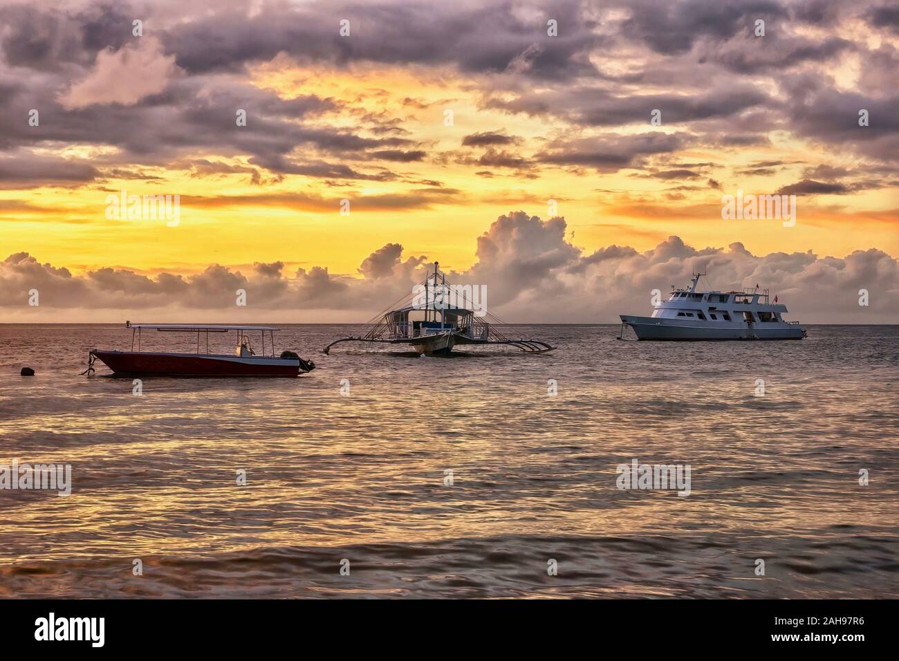 Un lever du soleil tropical, scène avec trois bateaux de touristes amarré dans un calme resort anchorage aux Philippines. Banque D'Images