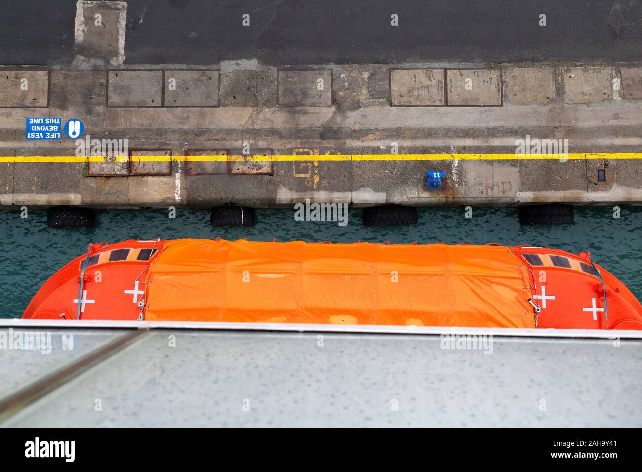 En regardant un quai dans le port de Limassol à Chypre. Une orange couverts lifeboat dépasse du côté de la station d'expédition. Banque D'Images