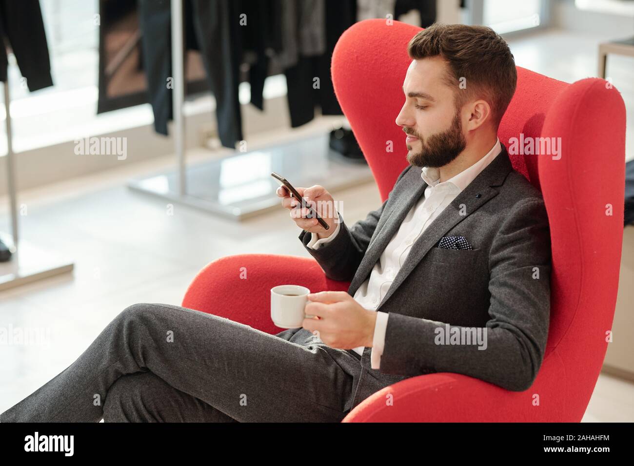 Jeune homme bien habillé avec tasse de thé des textos en smartphone Banque D'Images