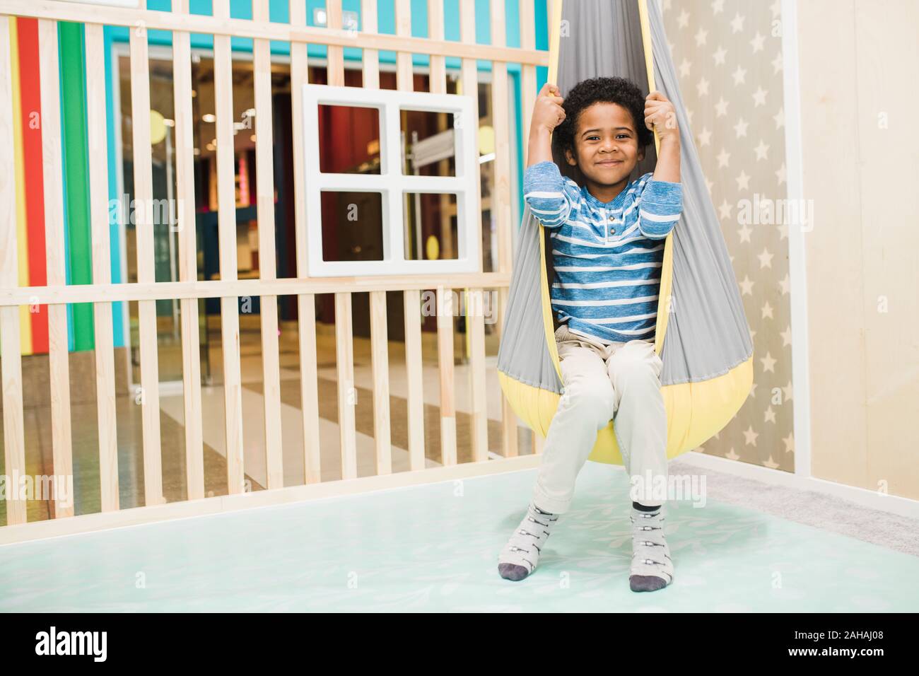 Happy little African boy dans casualwear assis dans un hamac suspendu au plafond Banque D'Images