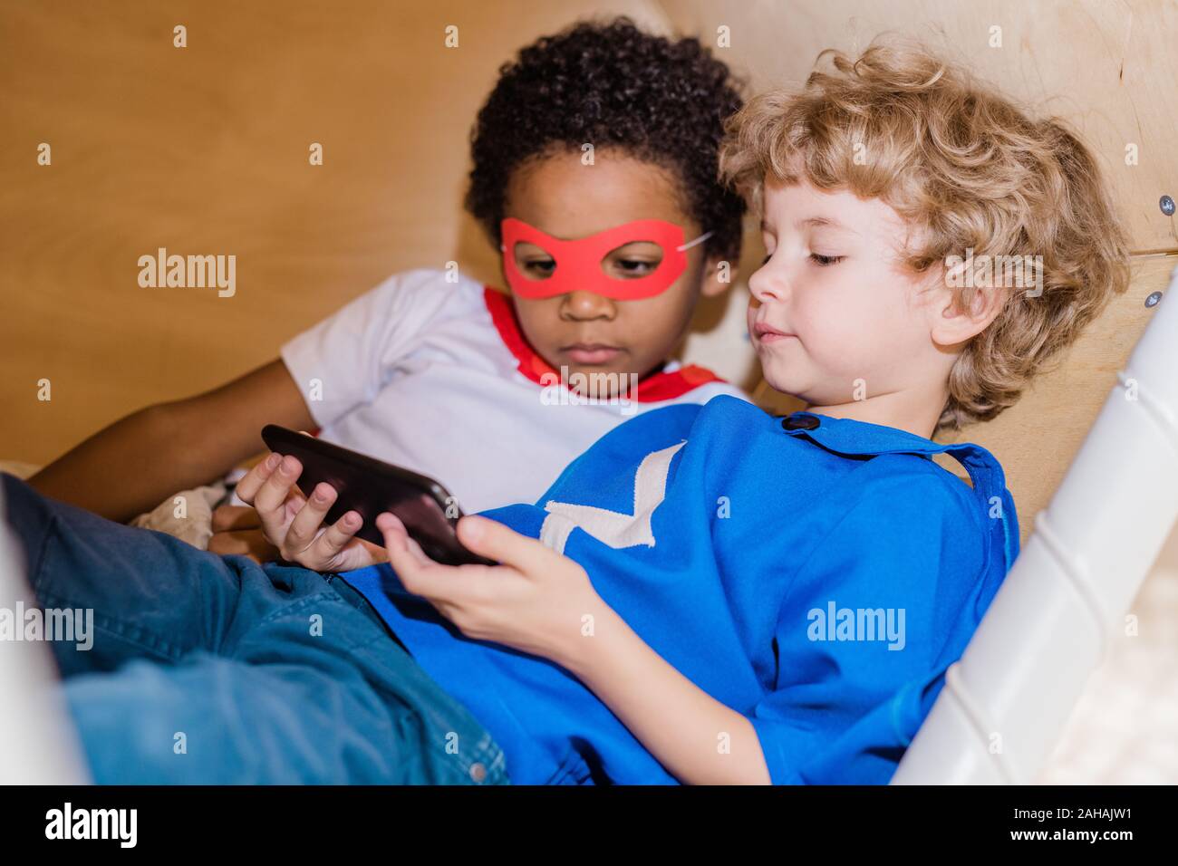 Deux garçons en costume de superman à l'écran de smartphone à tout en vous relaxant Banque D'Images