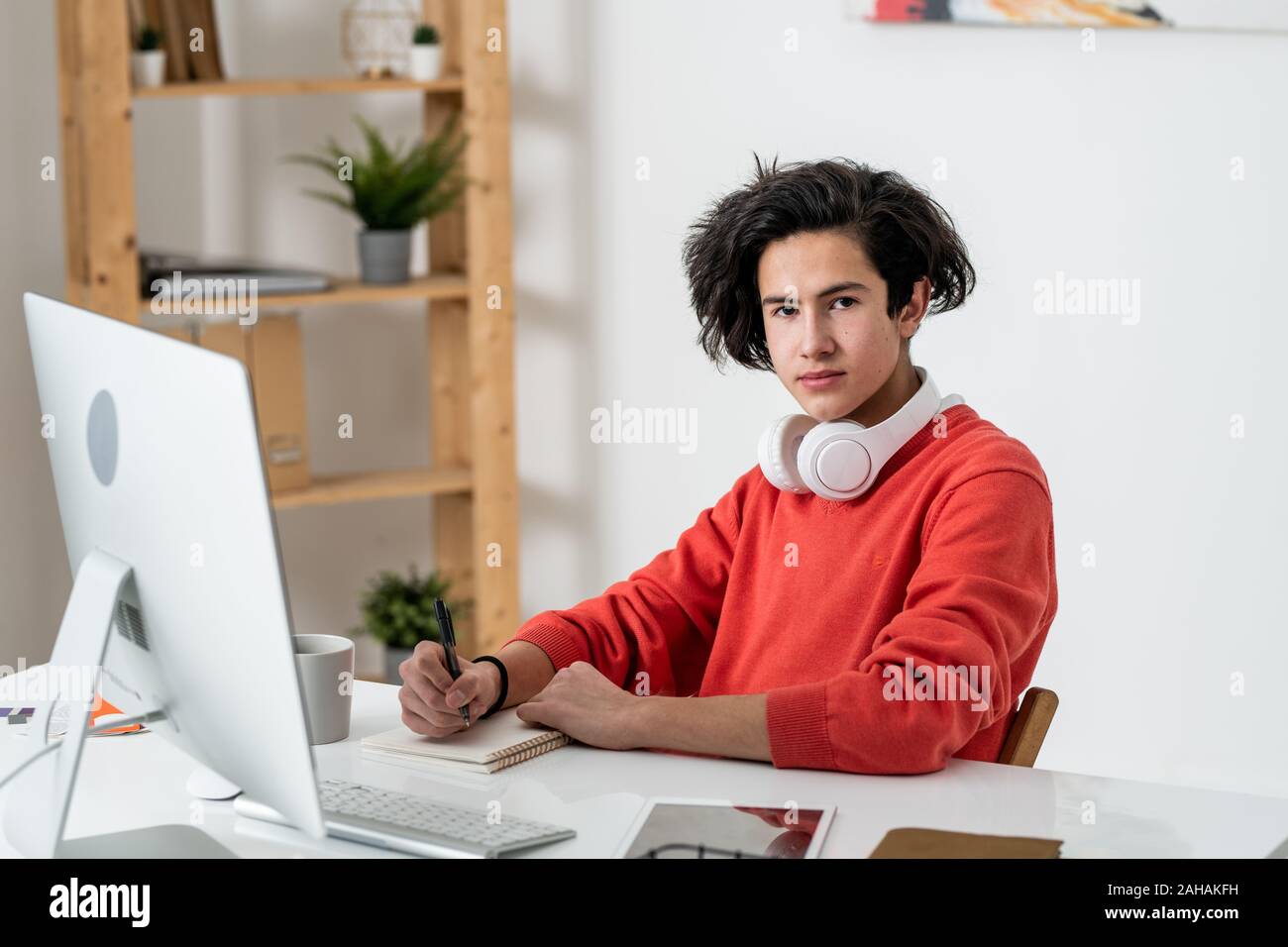 Young casual male freelancer vous regarde pendant que des notes par lieu de travail Banque D'Images