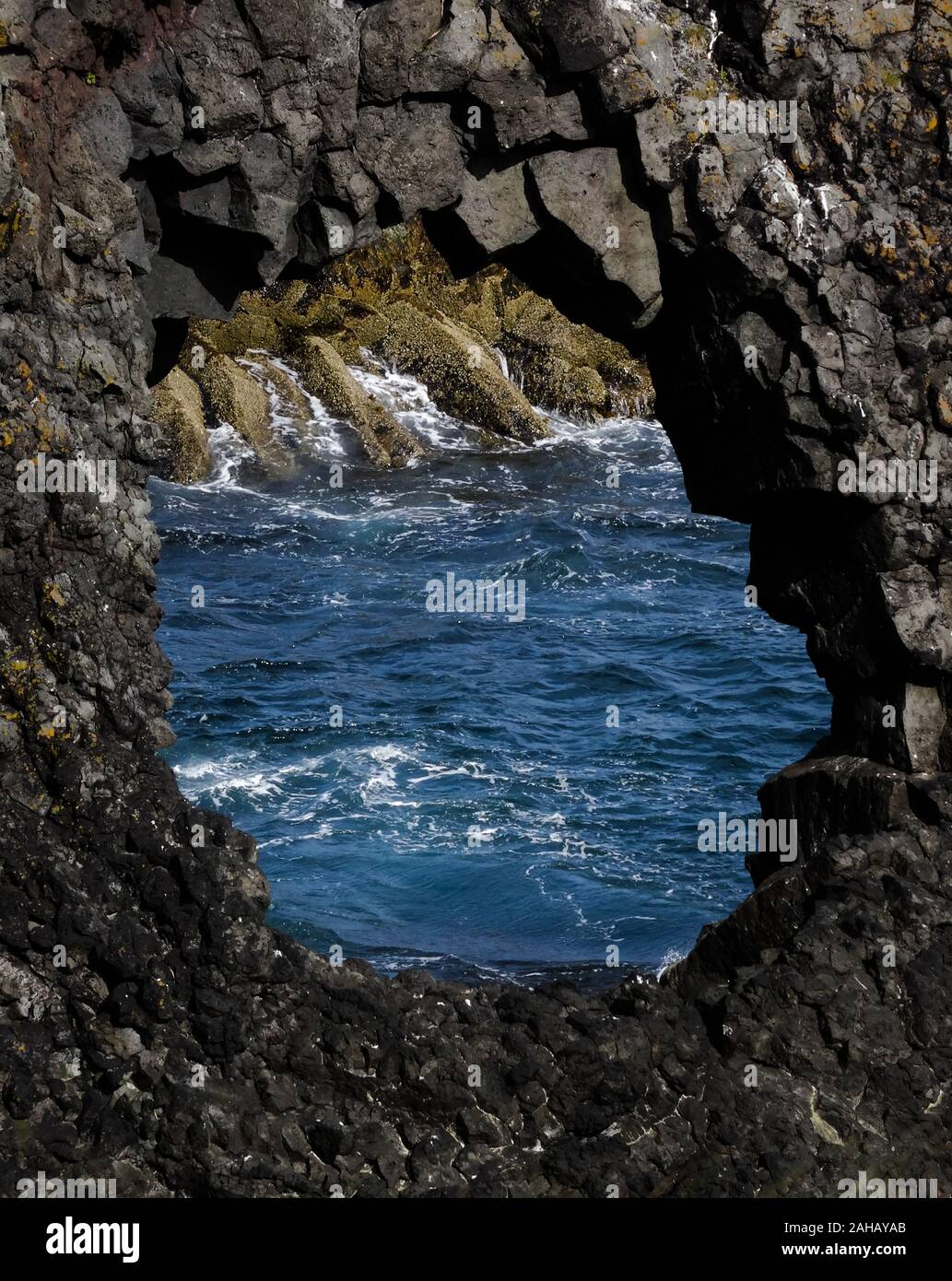 Trou dans la pierre de lave noire islandaise de la formation à l'océan atlantique en arrière-plan. Tourné près de Vik, Islande sur belle journée ensoleillée. Banque D'Images