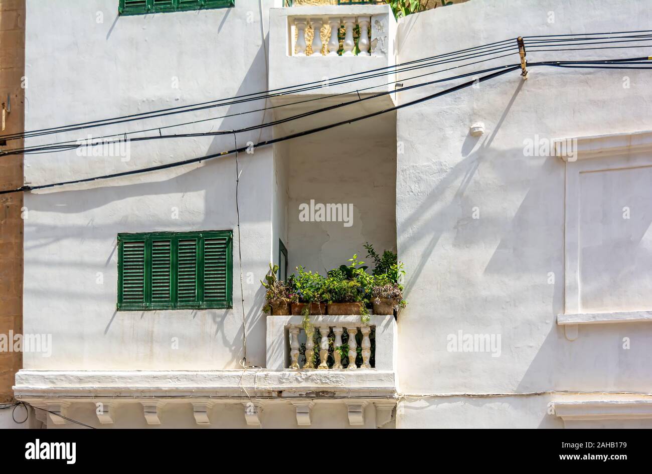 Fenêtre avec des volets fermés vert et d'un balcon avec des plantes en pots dans mur de pierre blanche à Sliema, Malte. Scène urbaine maltaise authentique. Banque D'Images