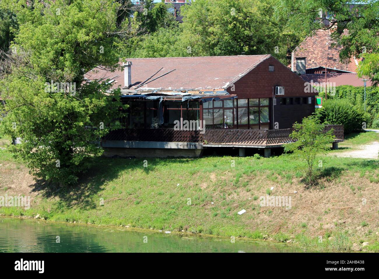 Abandonné petit restaurant avec de grandes terrasse avant et toit délabré détruit construit sur la rivière locale entouré d'herbe et dense Banque D'Images
