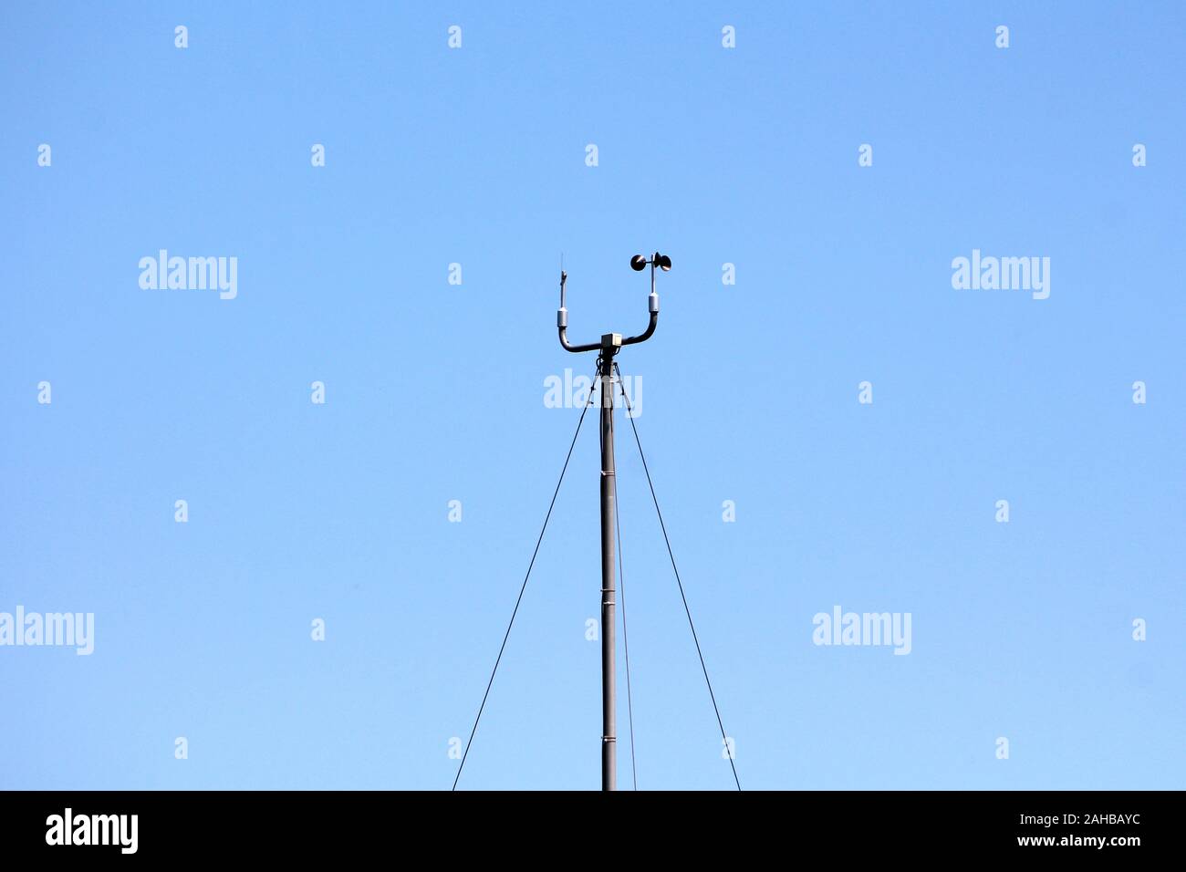 Vitesse et direction du vent instruments monté sur le dessus de grand poteau de métal détenu avec trois fils sur fond de ciel bleu clair Banque D'Images