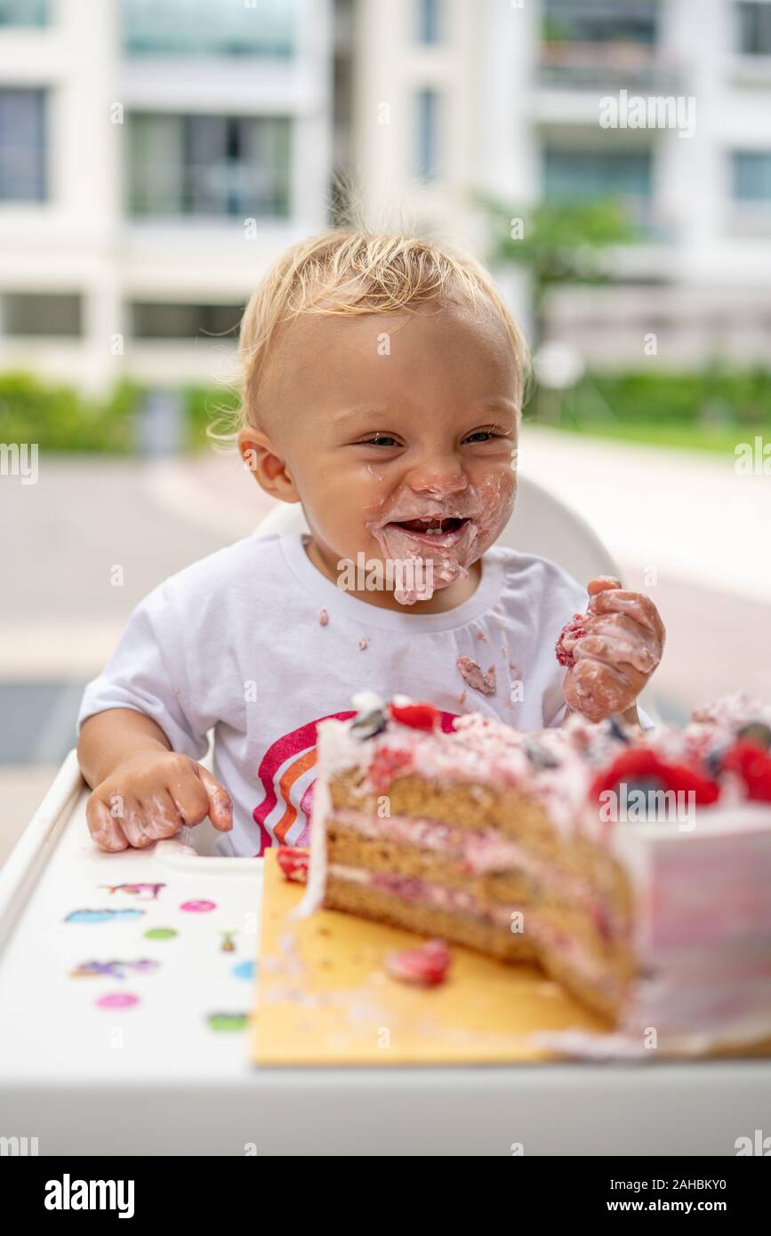 Un bébé qui mange son gâteau d'anniversaire savoureux avec ses mains avec du gâteau autour de la bouche Banque D'Images