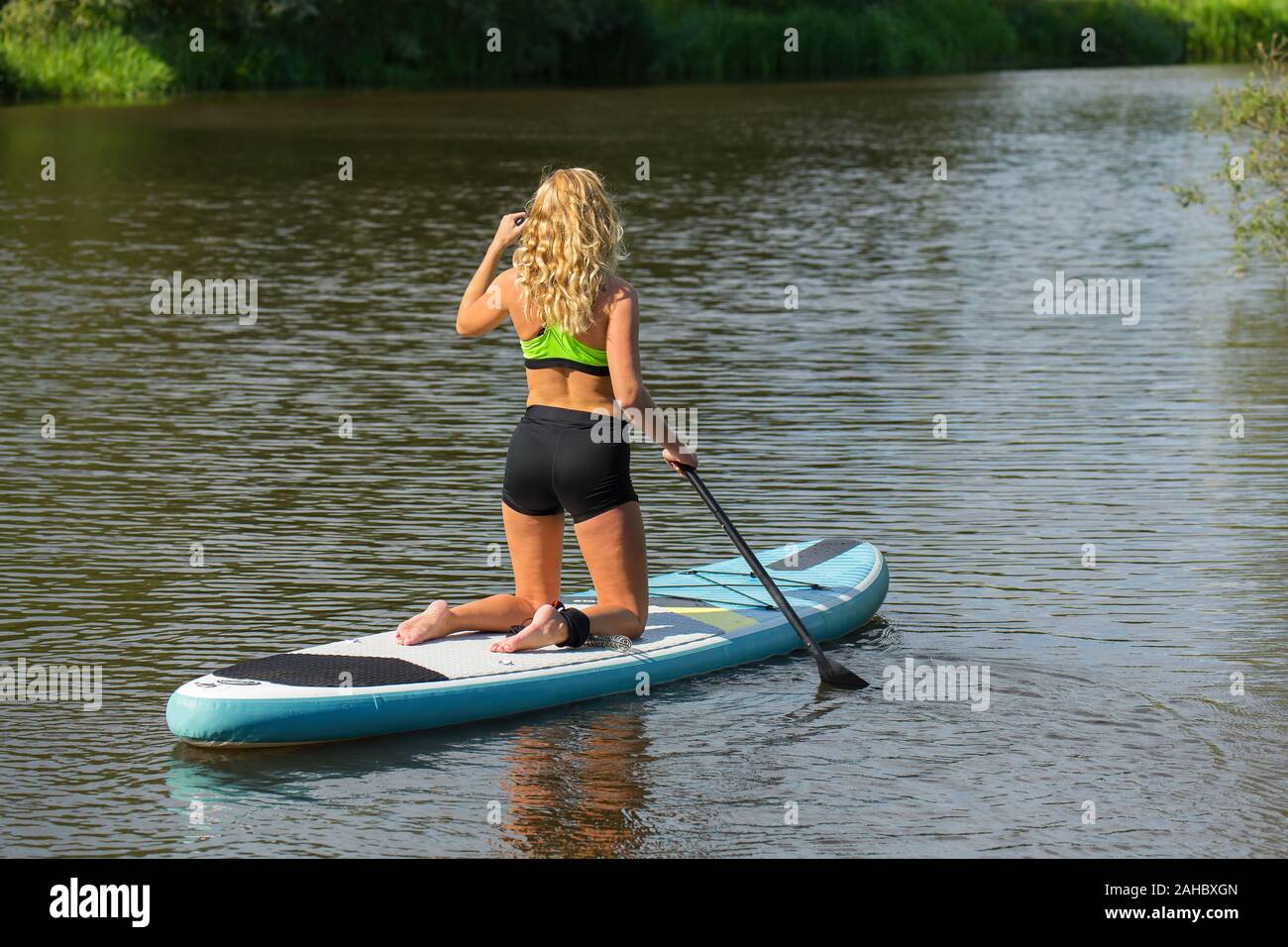 Jeune femme agenouillée avec pagaie paddle board sur l'eau de la rivière Banque D'Images