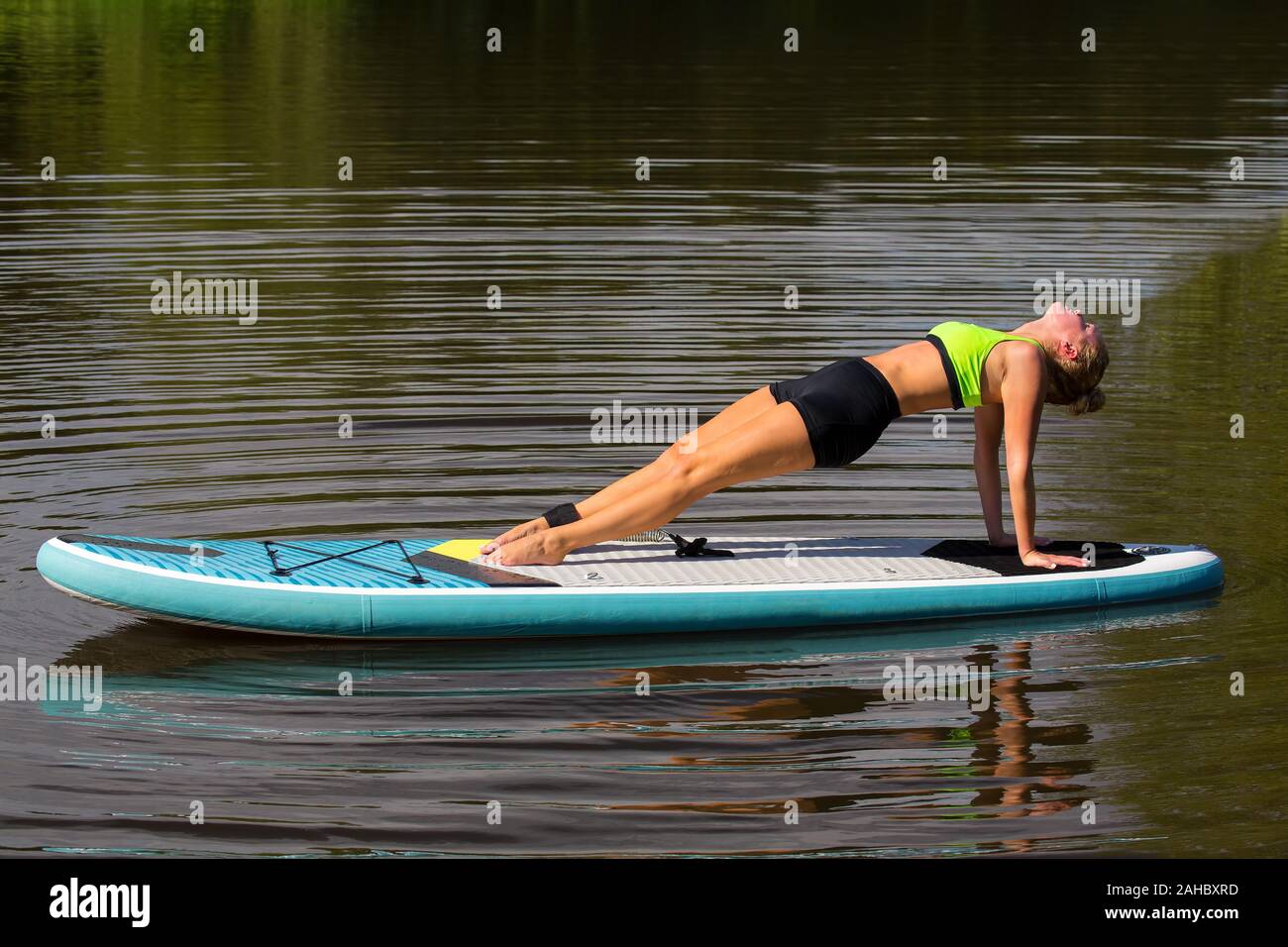 Young caucasian woman planking en arrière on paddle board au lac Banque D'Images