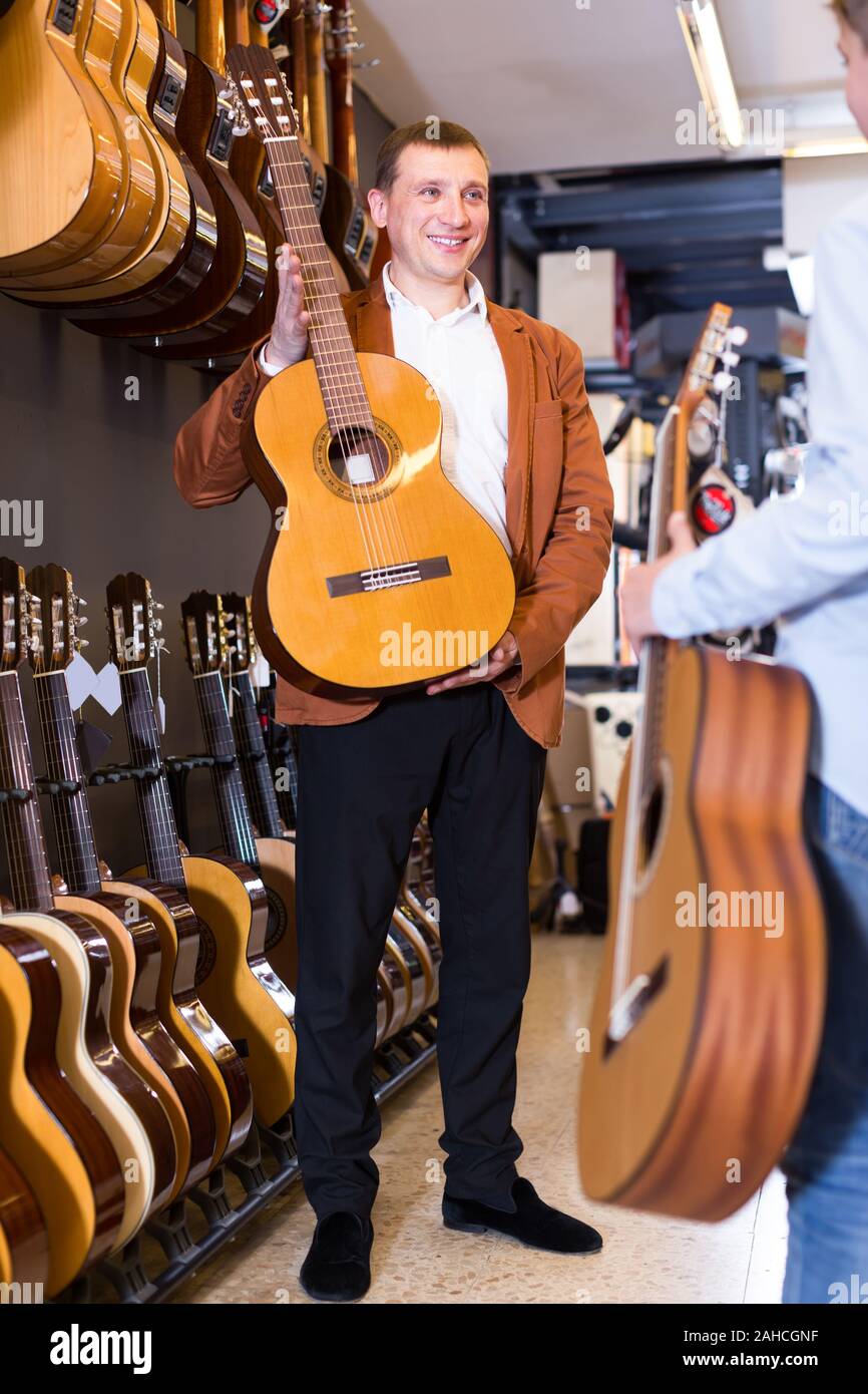 Vendeur masculin montre une guitare à six cordes classique dans un magasin de musique Banque D'Images