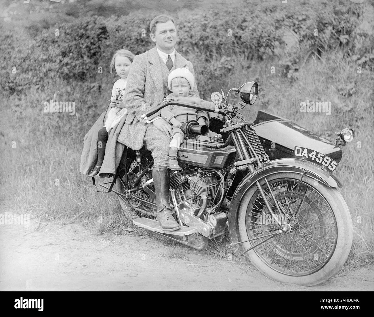 Une photographie vintage noir et blanc édouardienne montrant un homme suissant sur un vélo à moteur Royal Enfield, numéro de licence d'enregistrement, son DA 4595, avec sa jeune baie assise sur le réservoir à essence devant lui, et sa jeune fille assise derrière lui. Pris quelque part en Angleterre. Banque D'Images