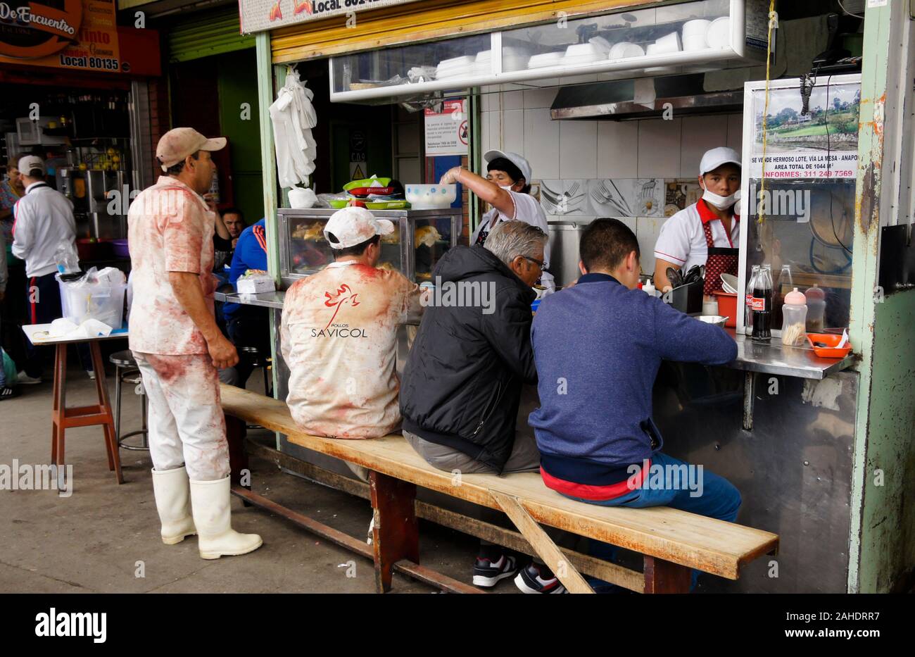 Les clients (y compris deux bouchers) manger à un stand dans le marché alimentaire Paloquemao, Bogota, Colombie Banque D'Images